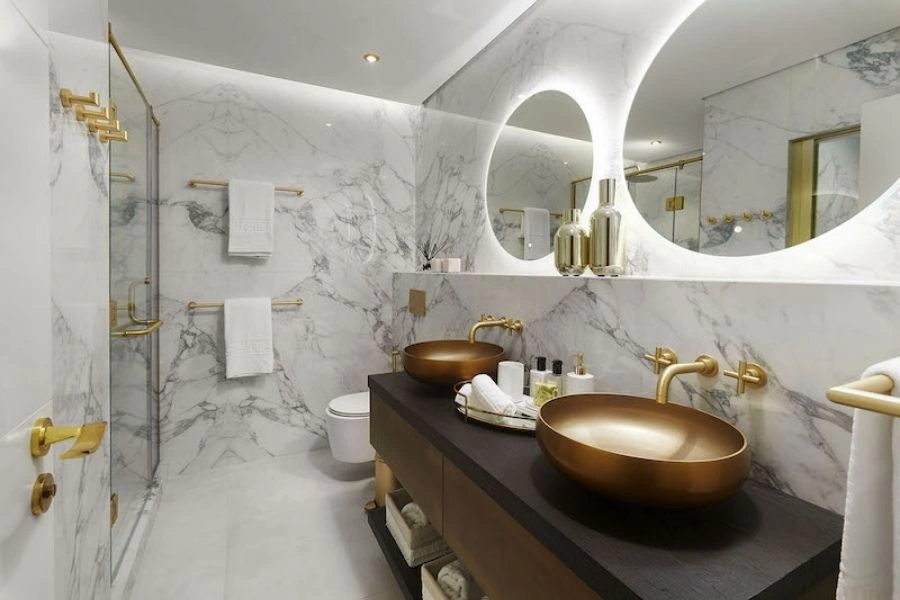 White marble bathroom with gold round sinks.