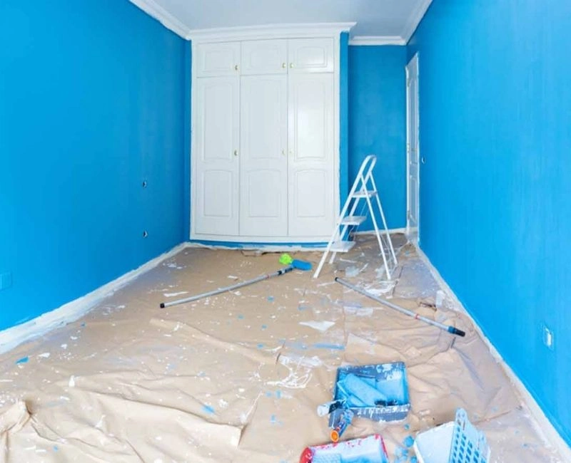 Messy room with blue paint on walls and floor covered in tarps.