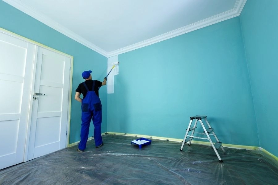 Professional painter applying light blue paint to a room wall.