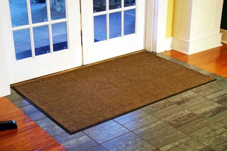 Brown indoor entrance floor mat on a tiled floor near a white door.