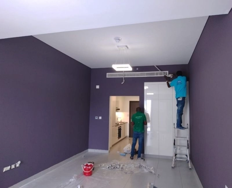 Professional painters working on a purple accent wall in a Dubai apartment.