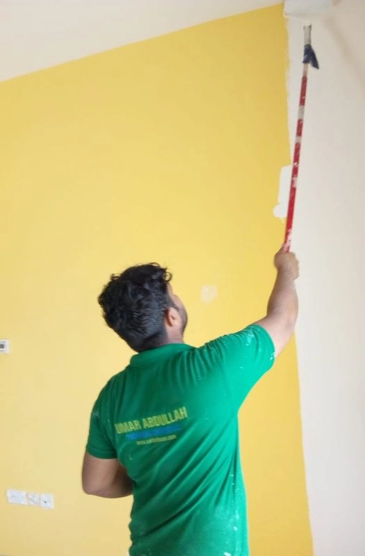 Professional painter in a green shirt painting a wall with yellow color.